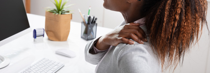 Woman at work with her hand on the shoulder indicating pain.