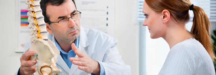 A professional pointing at a spine model while speaking to a patient.